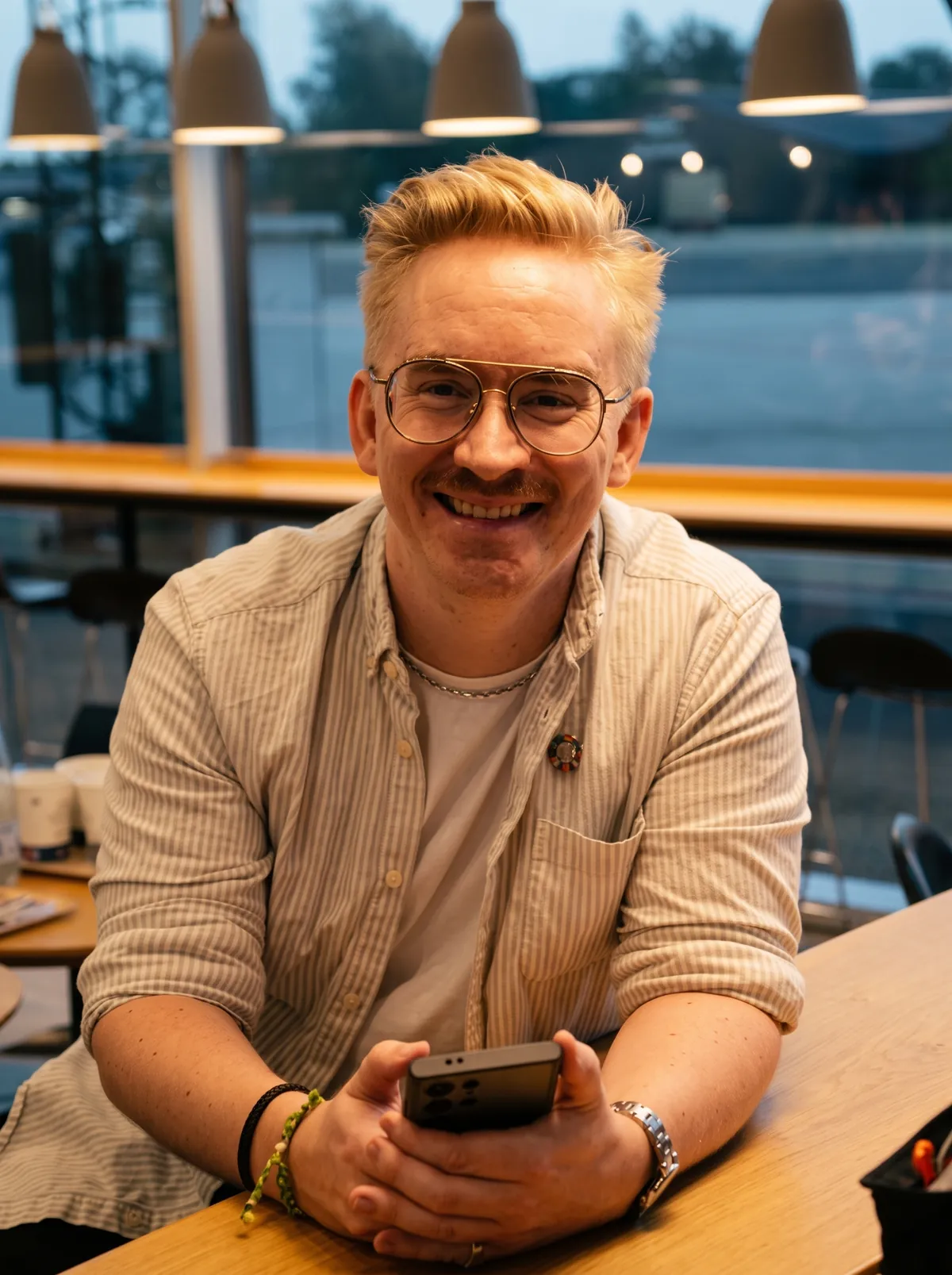Anders smiler og sidder ved et bord med sin telefon i hænderne.